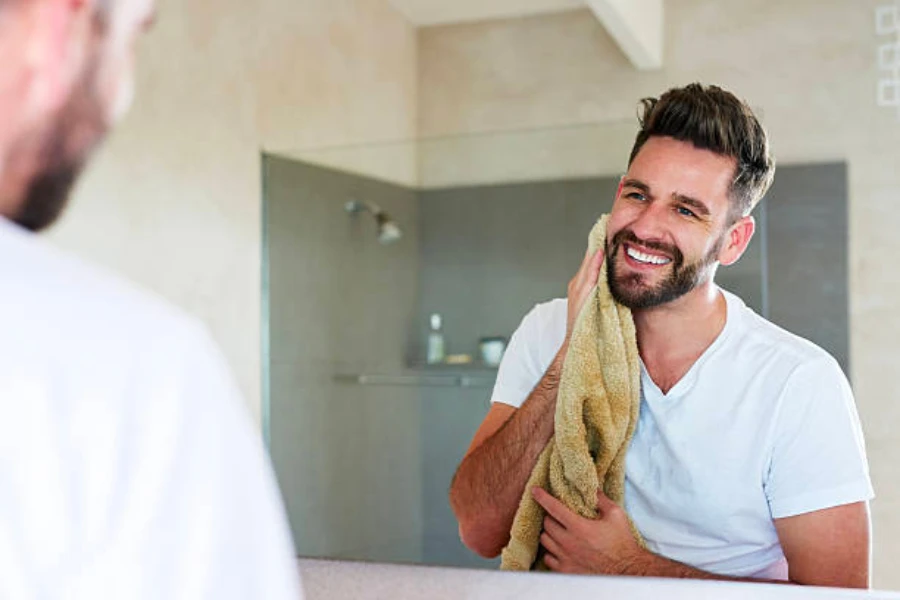 A man looking in the mirror and drying his face with a towel