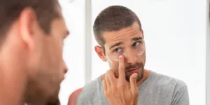 A man looking in the mirror applying undereye cream