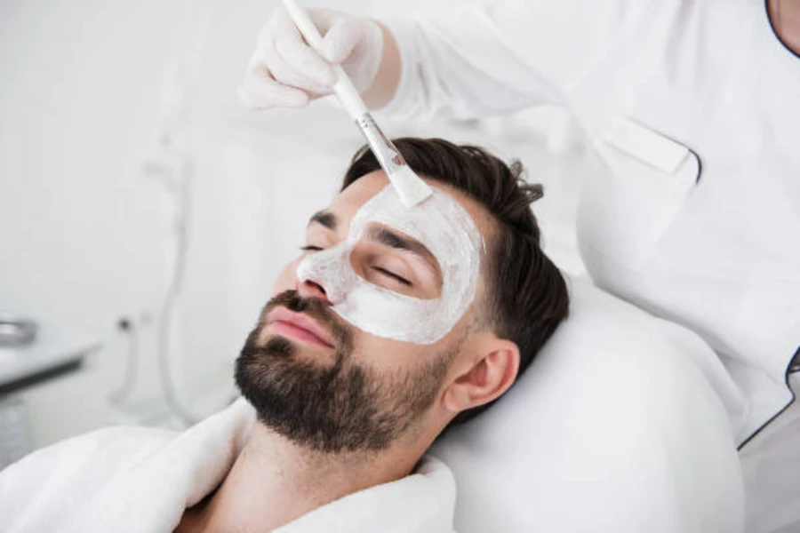 A man lying down having a facemask applied to his skin