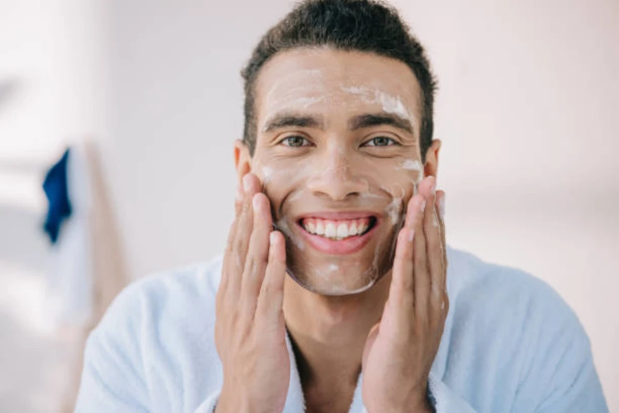 Un hombre sonriendo y aplicando crema facial con las manos.