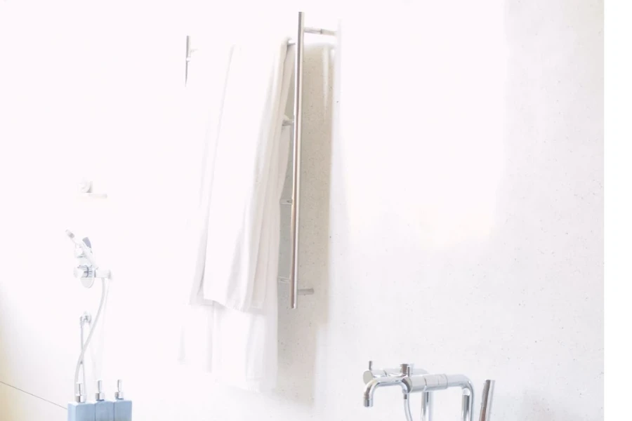 A stainless steel towel warmer with a white towel and bathtub