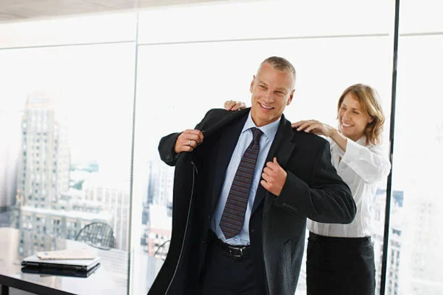 A woman helping a co-worker put on an overcoat