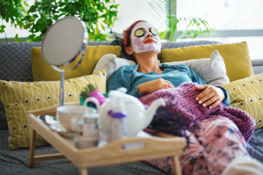 A woman laying on her couch with a facial mask on and cucumbers on her eyes