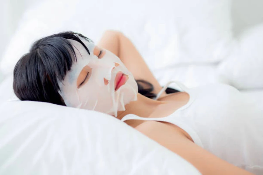 Seorang wanita berbaring di tempat tidur dengan masker perawatan kulit di wajahnya