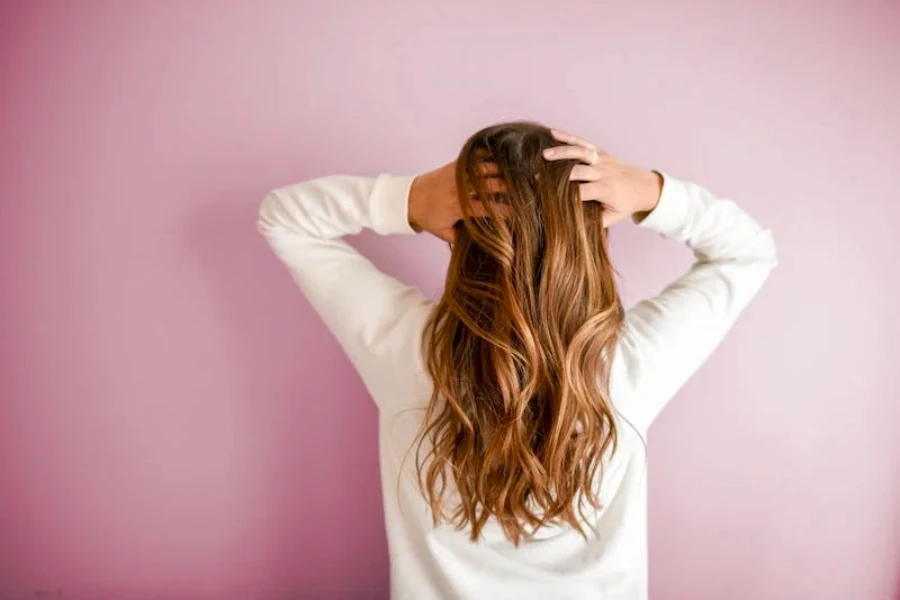 A woman running her hands through her hair with a pink background