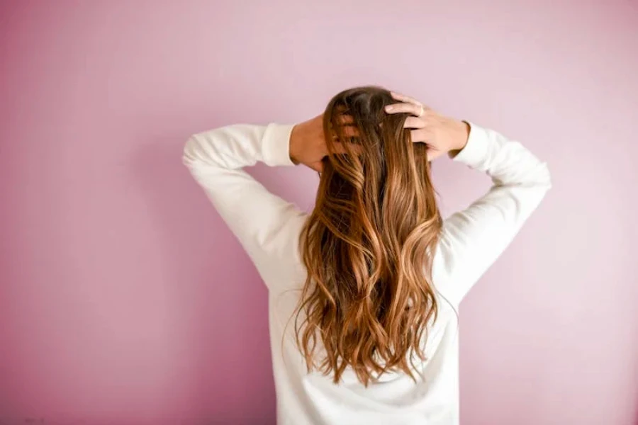 Eine Frau fährt sich mit den Händen durchs Haar, vor rosa Hintergrund