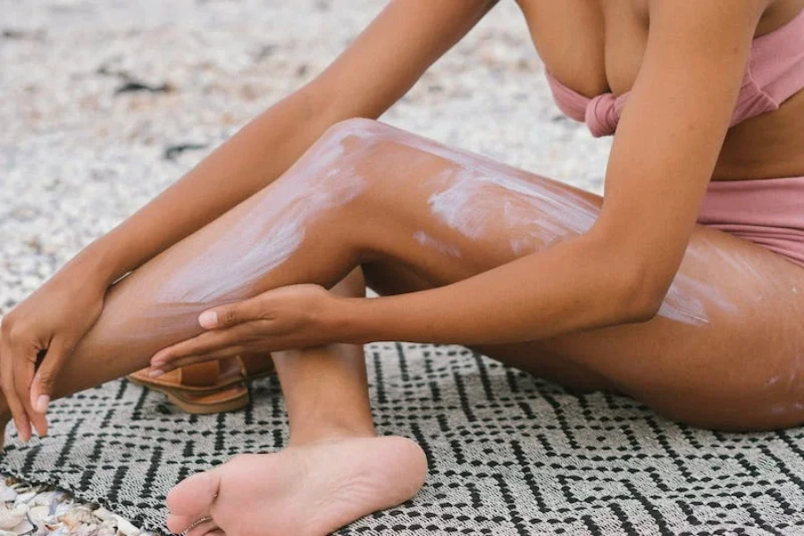 A woman sitting on the beach applying sunscreen