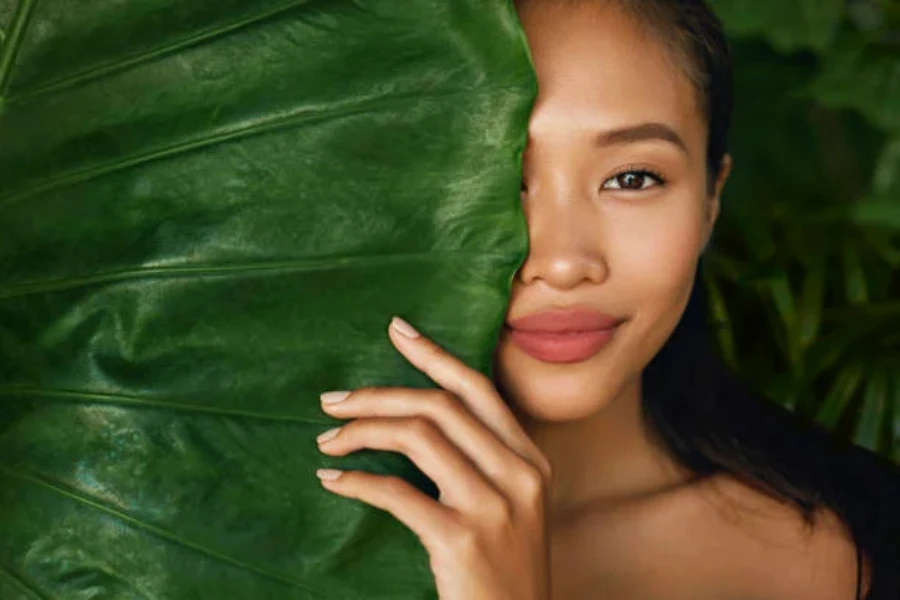 A woman standing behind a large green leaf hiding half of her face