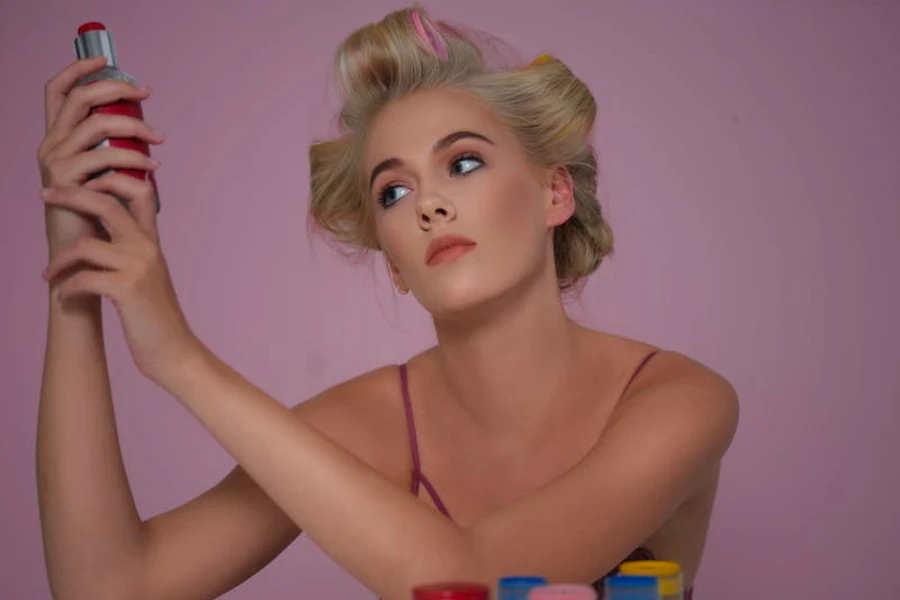 A woman with curlers in her hair looking at the ingredients on a bottle