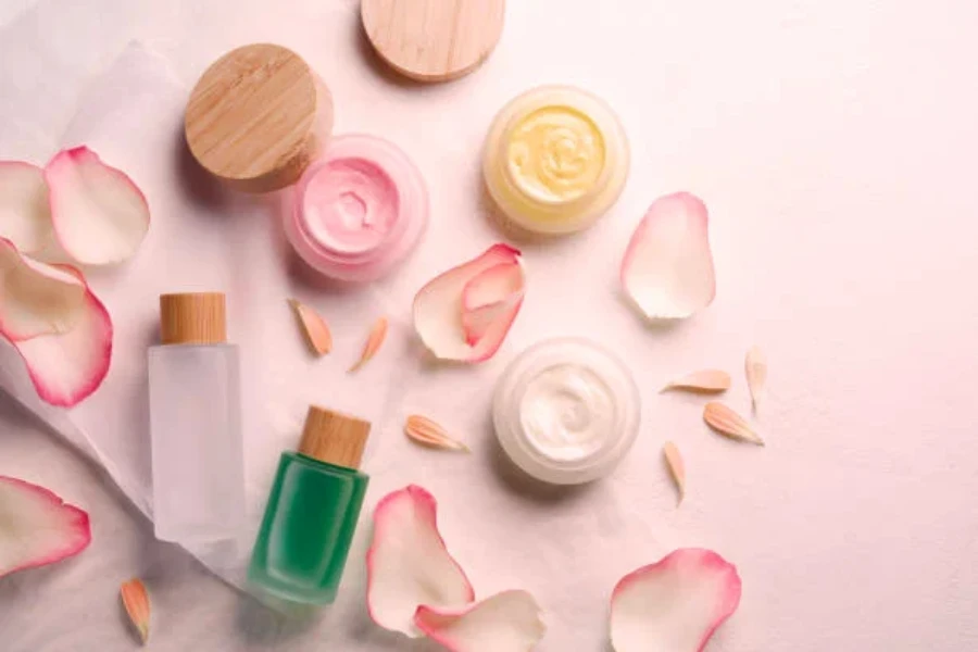 Three jars of skin care cream and two bottles of liquid with pink rose petals around them