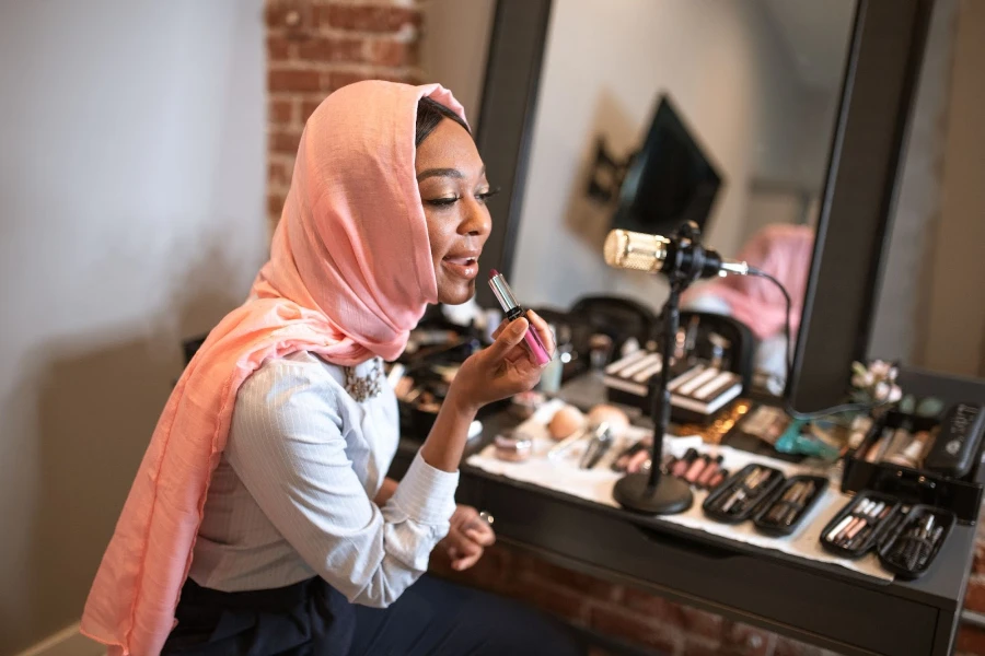 A woman wearing a hijab putting on lipstick