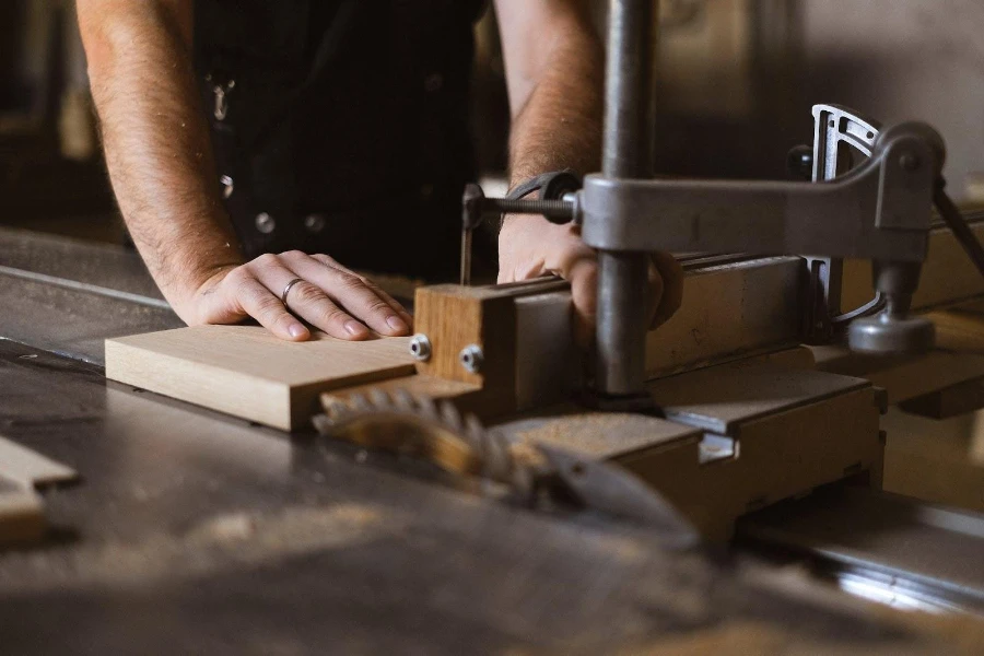 A man using an automated saw to cut a thick wooden lumber