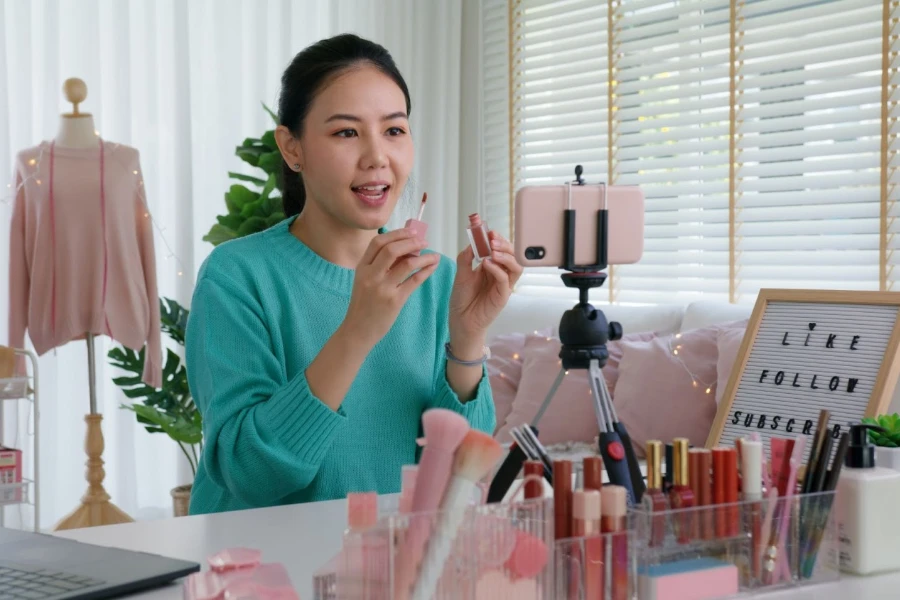 A woman influencer is using her phone to livestream a makeup tutorial from her home