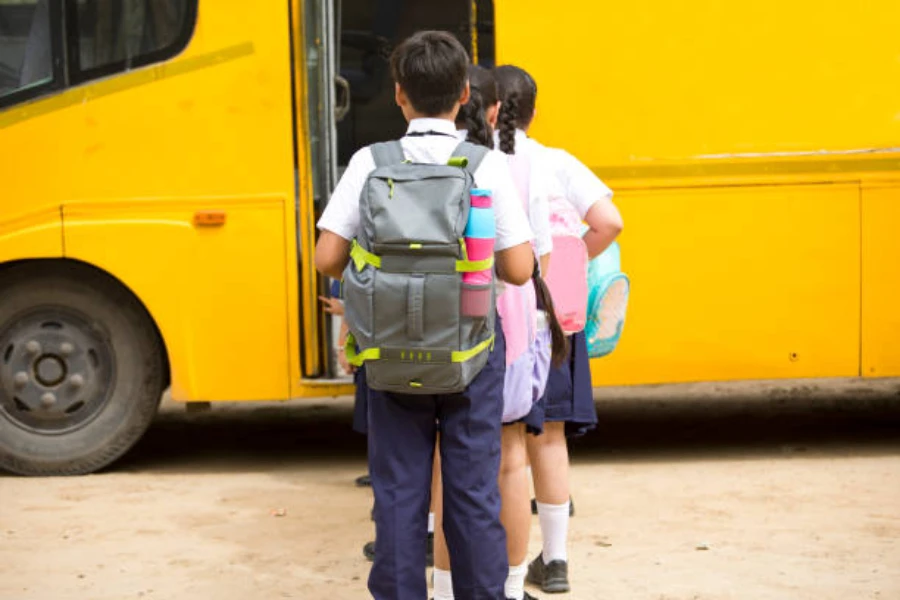 Ragazzo in attesa di salire a bordo dell'autobus giallo con zaino impermeabile