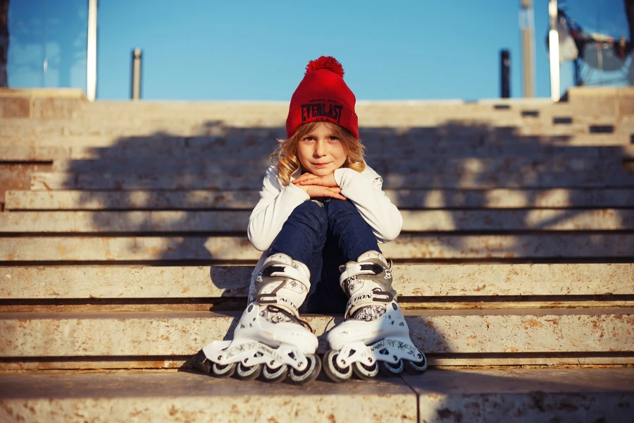 Criança sentada nos degraus ao ar livre usando patins em linha brancos