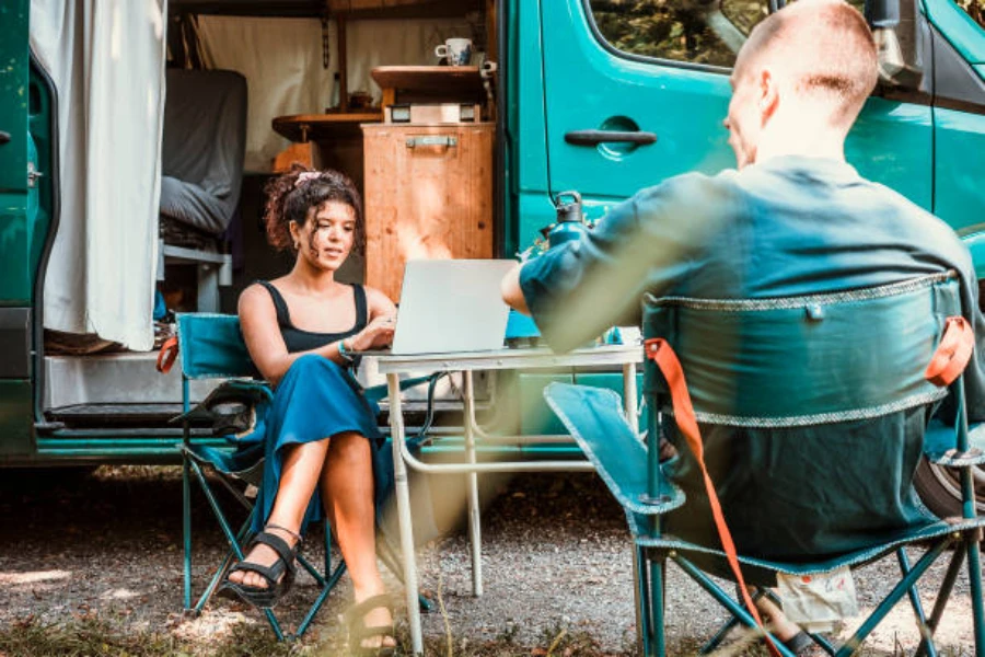 Couple sitting outside camper van with folding table and chairs