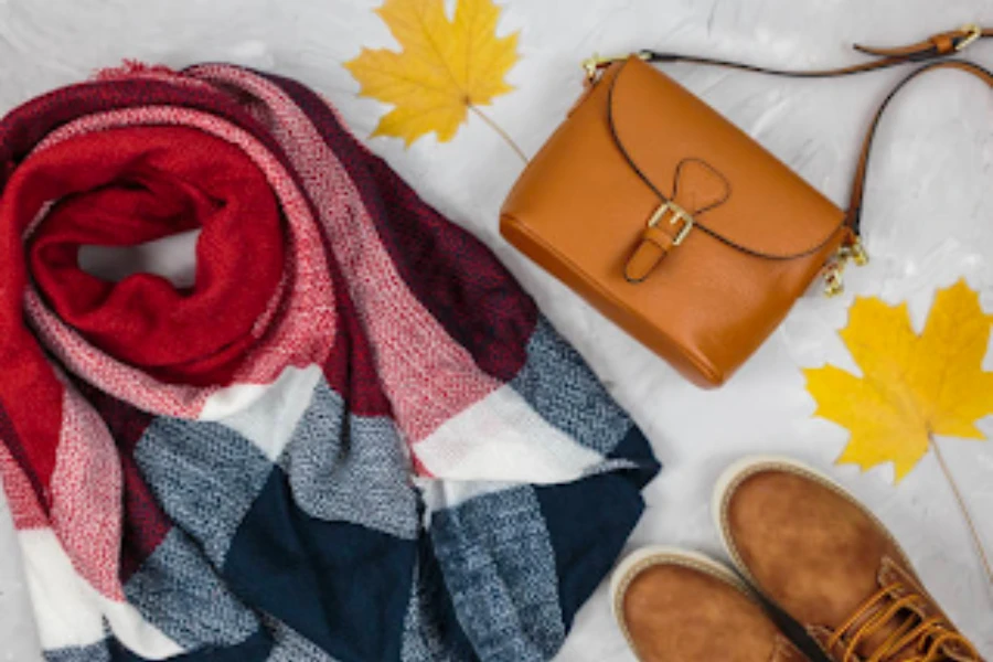 Fall accessories laid out on white background with autumn leaves