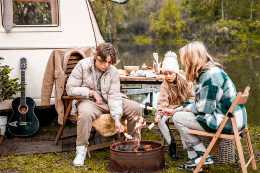 Family of three making s’mores around fire outside of van