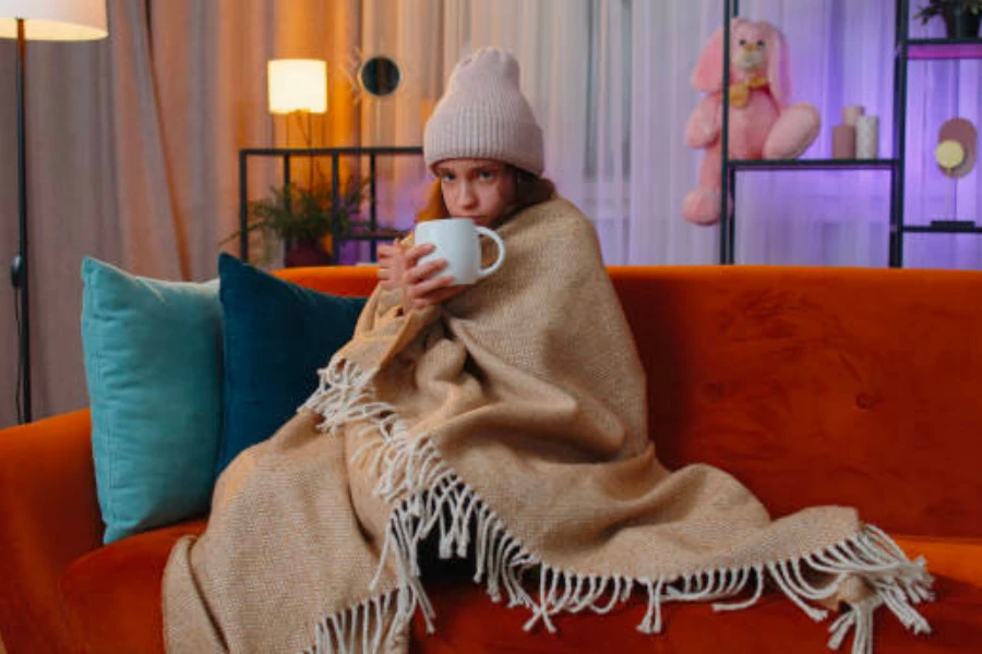 Girl wearing a winter hat and blanket while holding a mug