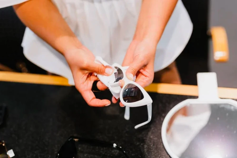 Person holding cream white sunglasses and cleaning the lenses