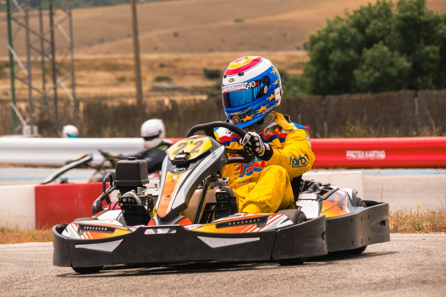 Professional go kart driver in yellow jumpsuit and helmet rounding a track