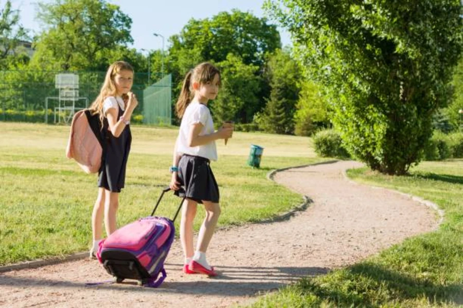 Two girls walking through park with one rolling a backpack