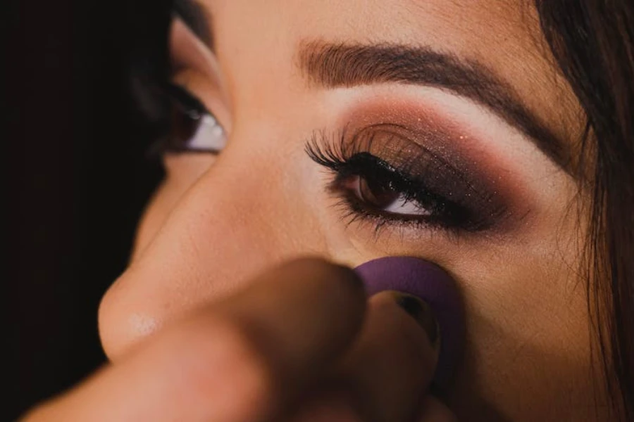 Mujer aplicando sombra de ojos marrón ahumado en la cara