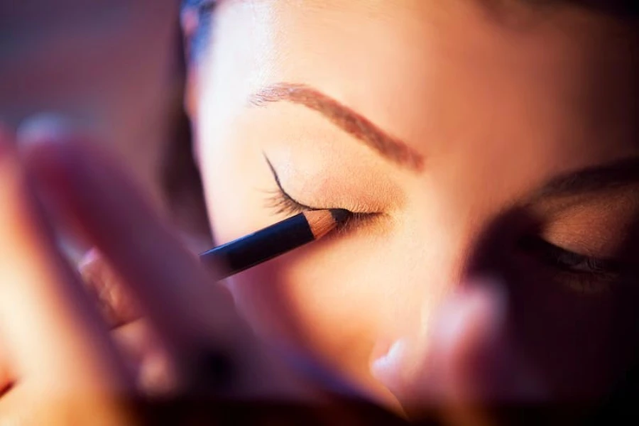 Woman drawing sketchy wings to her eyelids with eyeliner