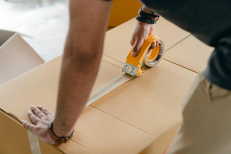 A man taping the middle of a cardboard box for shipping