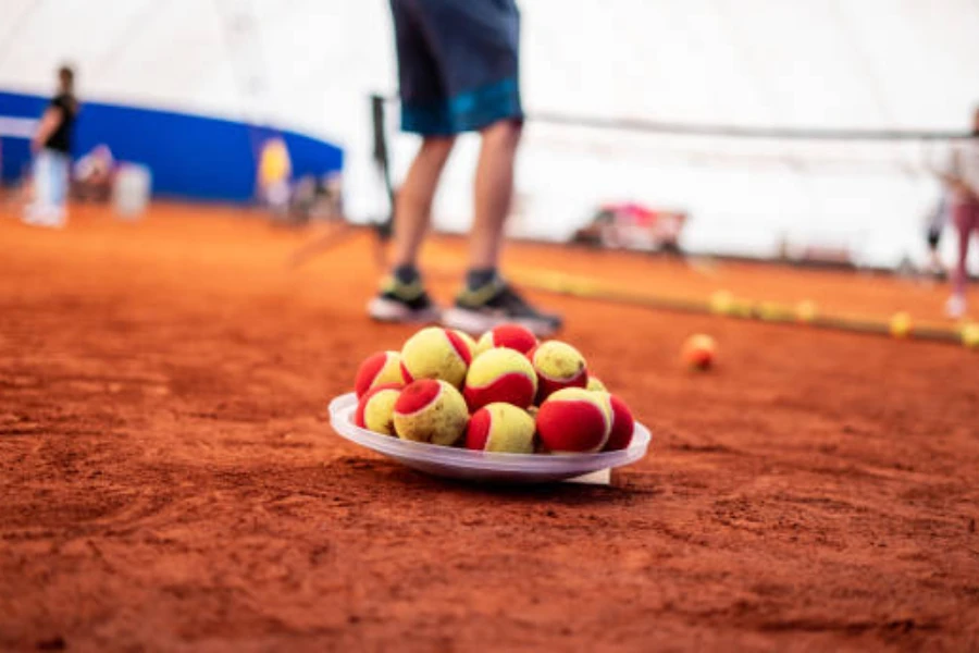 Clay court with bowl filled with red felt tennis balls