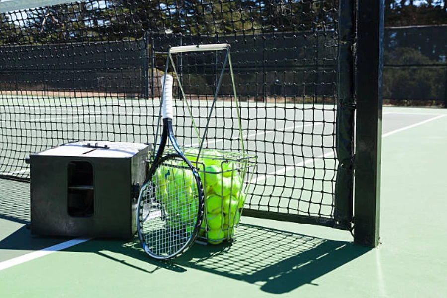 Grey tennis ball machine next to outdoor tennis net