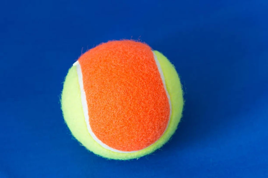 Orange felt tennis ball sat on blue painted ground