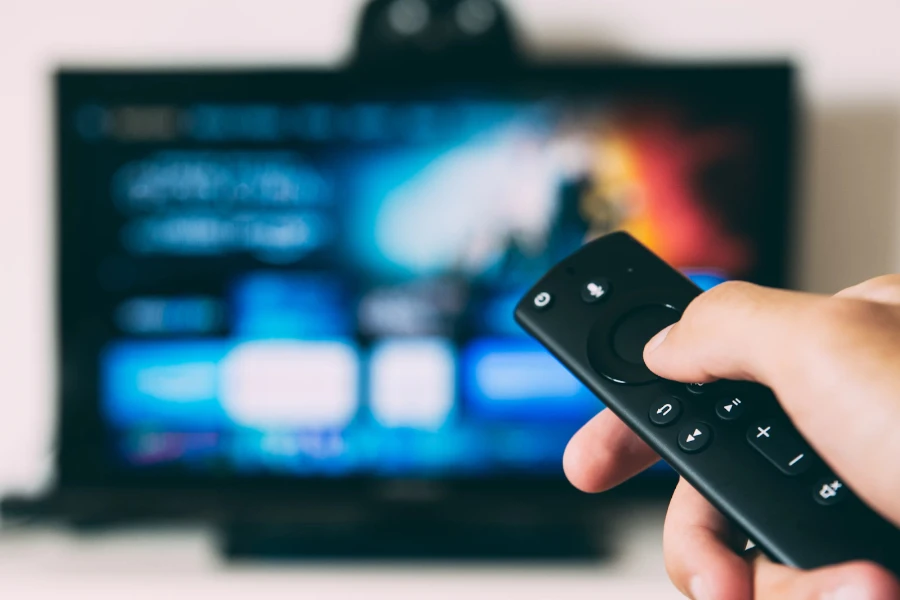 person holding a remote in front of a blurry TV