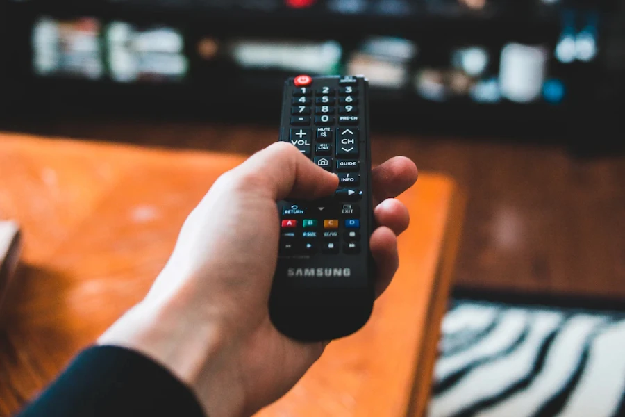 remote in a person's hand pointed at a TV that's blurry in the background