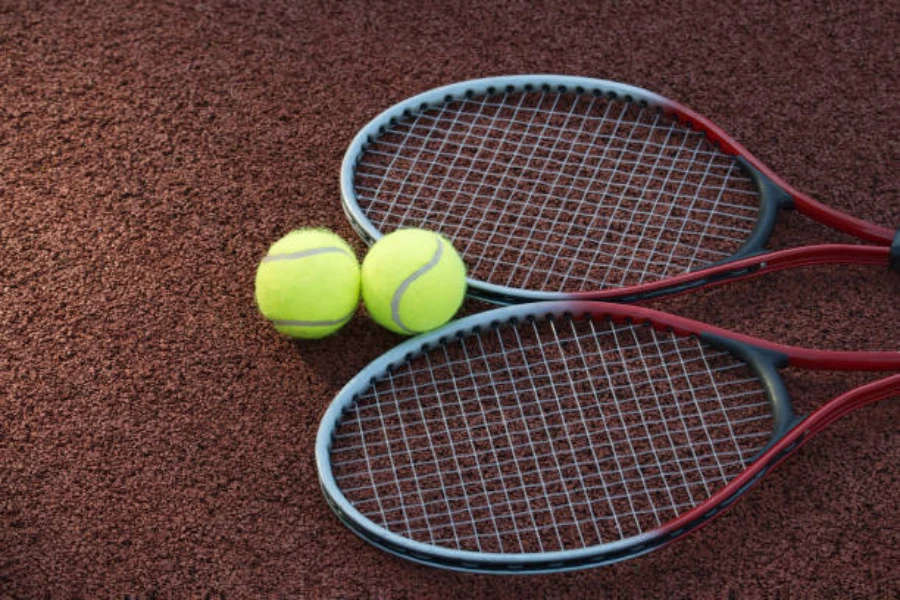 Two tennis racquets lying on court with two tennis balls